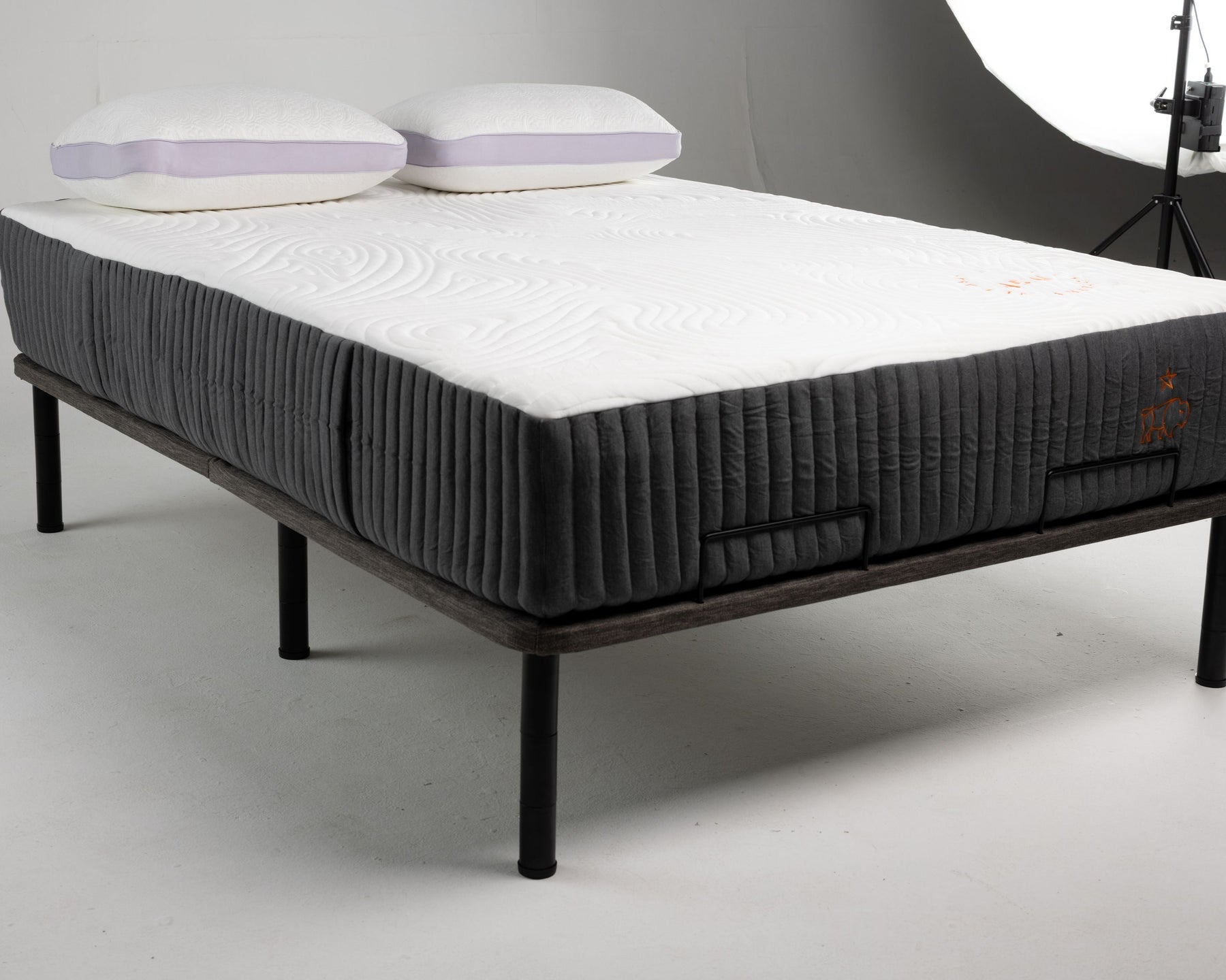 Mattress on a bed frame with pillows on a gray background